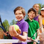 Close-up portrait of smiling active family, holding tennis rackets and ball on the court in sunny day